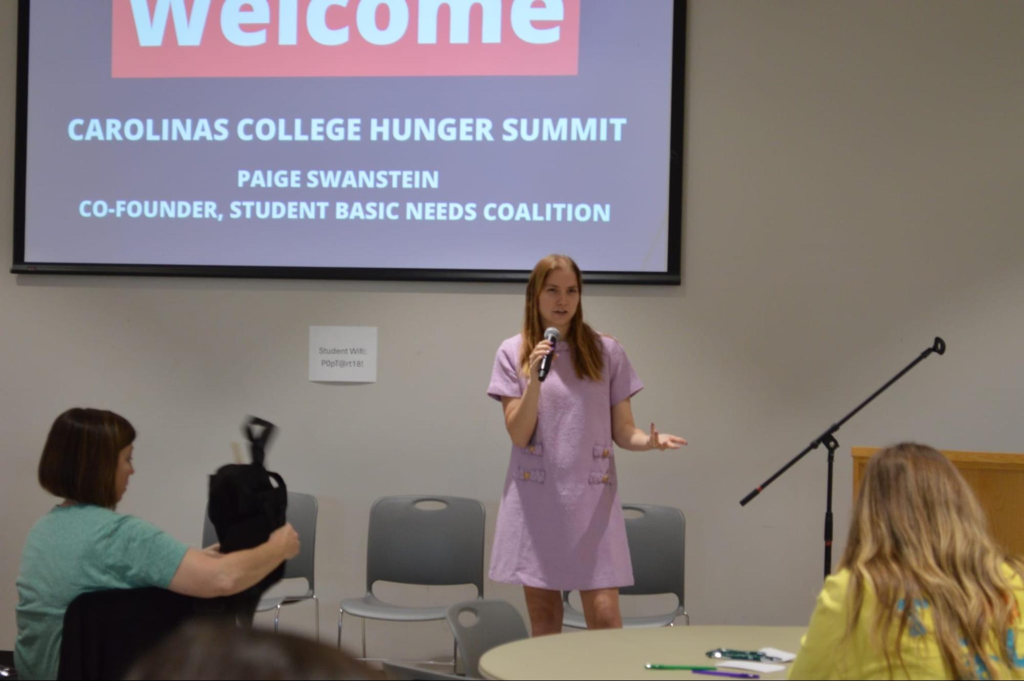 Woman speaking at the Carolinas College Hunger Summit with event title projected behind her.