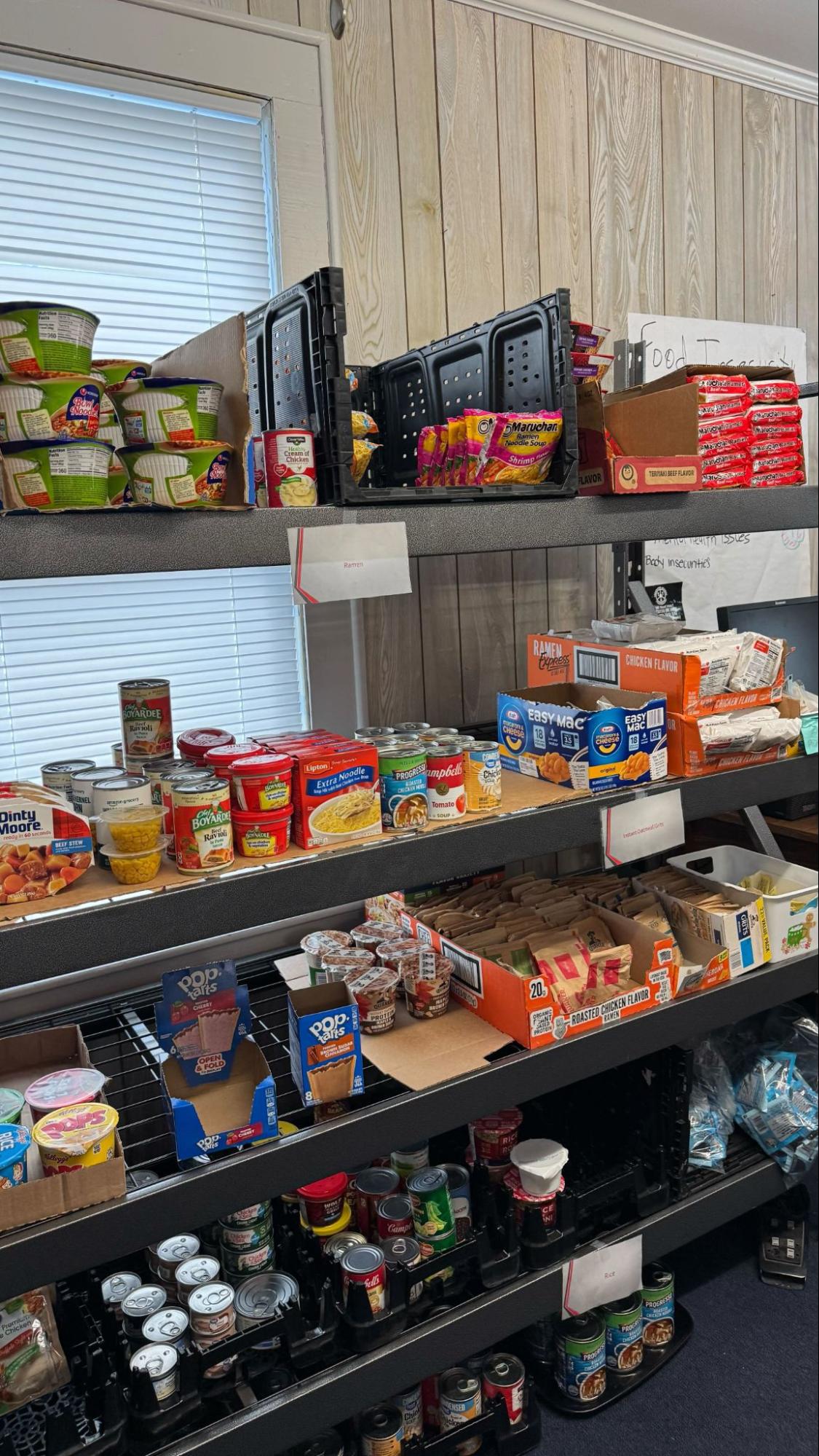 Shelves stocked with canned goods, instant noodles, and snacks in a campus food pantry.