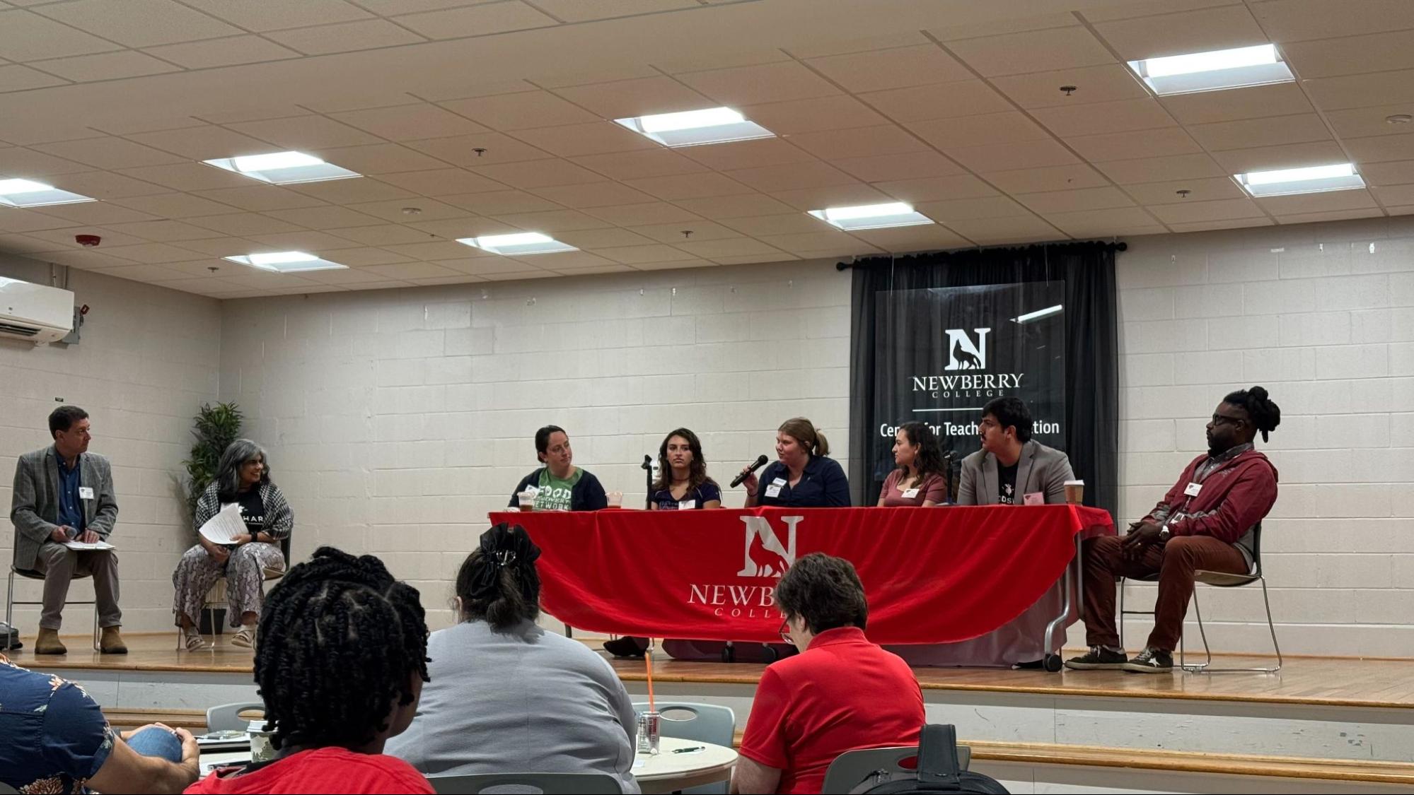 Six panelists speak at a table with microphones during a session.