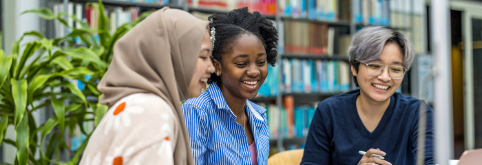 Three undergrad college students talking and laughing together in an academic library.