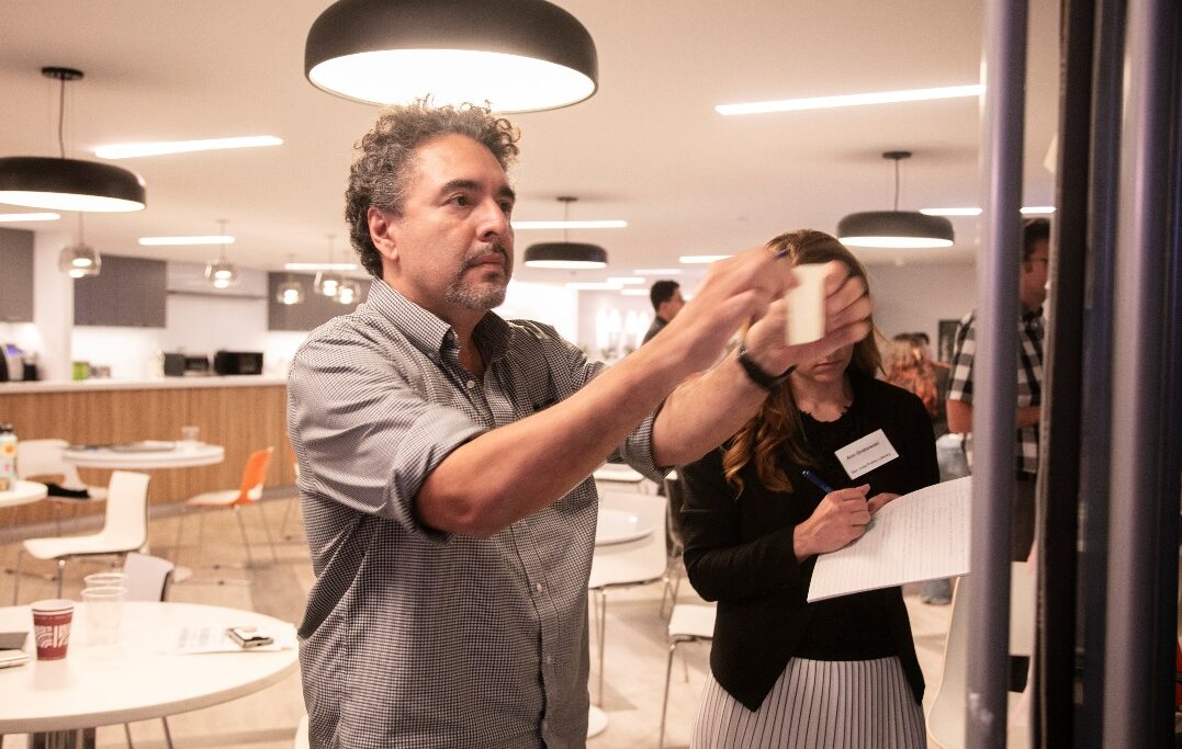 Two participants place sticky notes on posters in modern, brightly light office gathering space. 